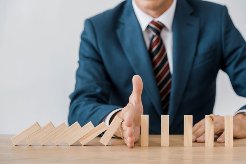 stopping-dominoes-wiht-hand man stopping dominoes from falling with hand wearing suite